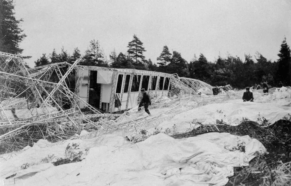 Die historische Aufnahme zeigt das Wrack eines Luftschiffs. Die Hülle liegt auf dem Bodenverteilt und Gerippe ist zertrümmert. 