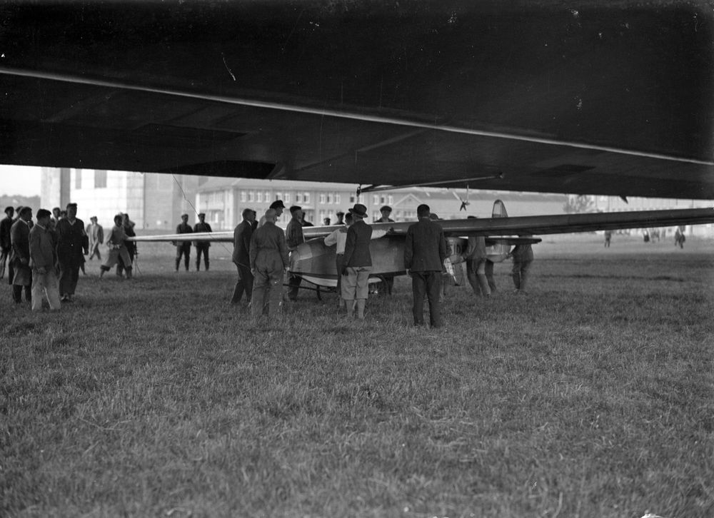 Historische Fotoaufnahme einer Gruppe von Männern, die um ein kleines Flugzeug herum stehen.