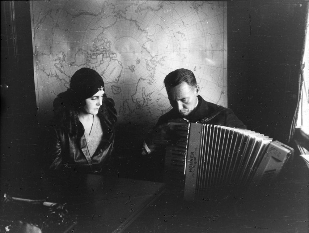 Die Aufnahme zeigt einen Mann und eine Frau, die nebeneinander sitzen. Der Mann spielt Akkordeon.