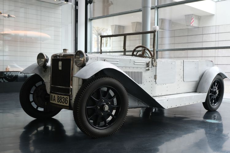 Der Wagen der Schwäbischen Hüttenwerke von 1925 im Zeppelin Museum. Er ähnelt einem Jeep mit einer silberfarbenen Aluminiumkarosserie. Im Hintergrund steht die Größenvitrine und man sieht die Straße zum Museum.